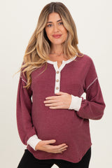 woman wearing a burgundy maternity top with button details and long sleeves, gently cradling her baby bump