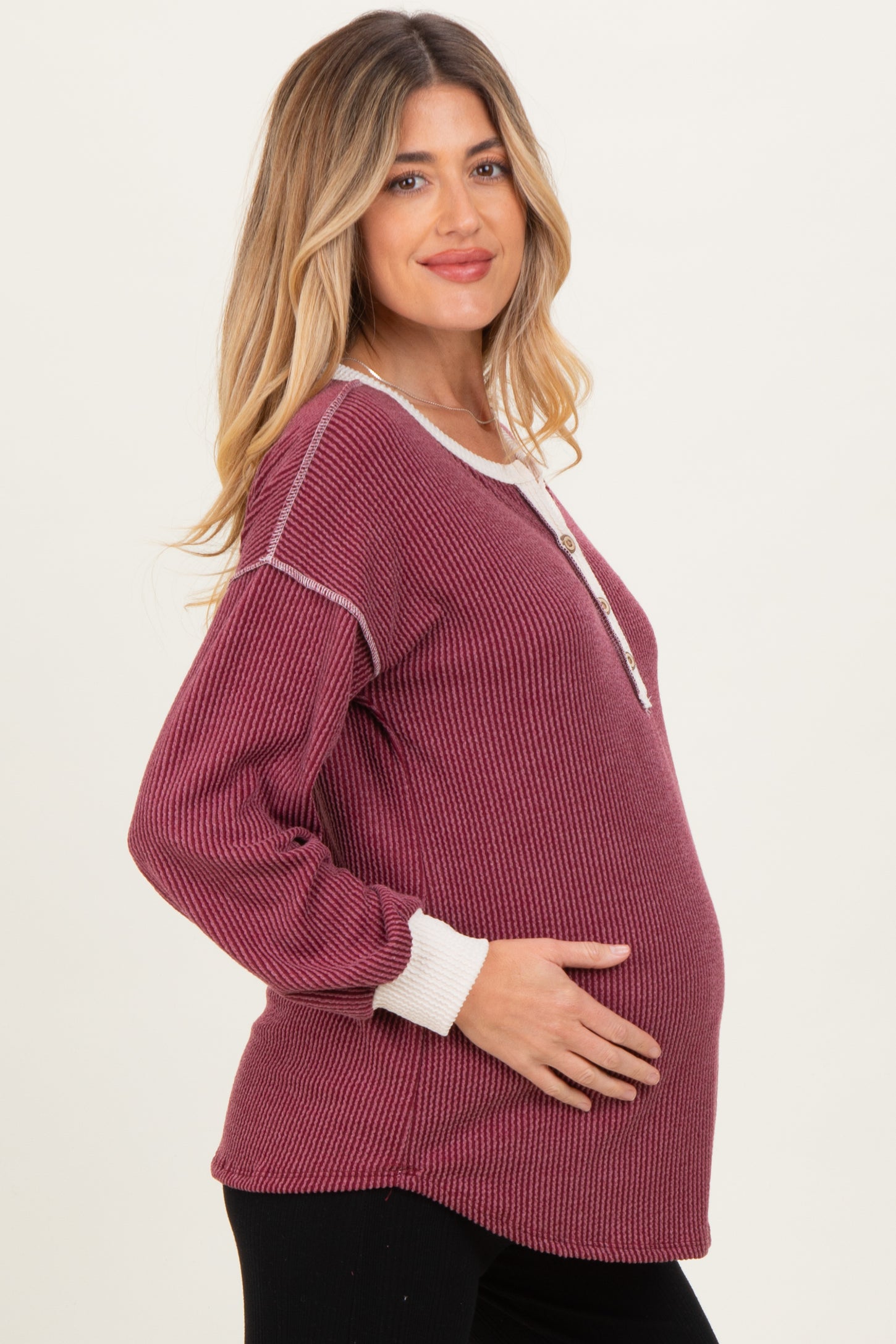 woman wearing a burgundy ribbed maternity top with a button detail and holding her baby bump
