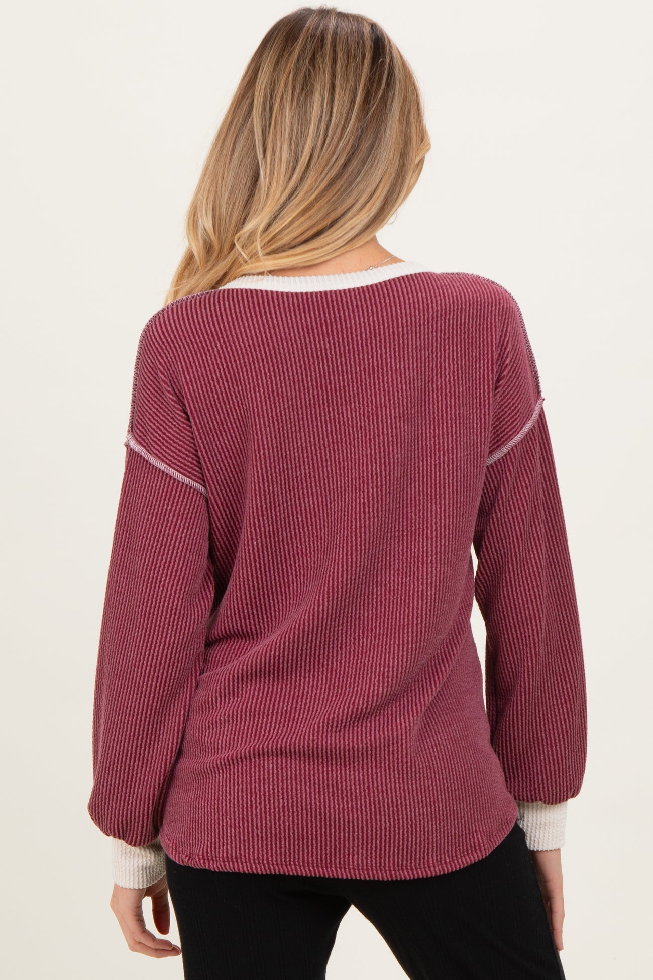 woman wearing a burgundy maternity sweater with striped details and balloon sleeves, showing the back view
