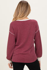 woman wearing a burgundy maternity sweater with striped details and balloon sleeves, showing the back view