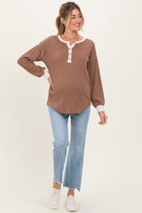 woman wearing a brown ribbed maternity top with white buttons and a white collar, paired with light blue jeans and white sneakers