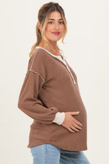 woman wearing a brown ribbed maternity sweater with white trim, cradling her baby bump