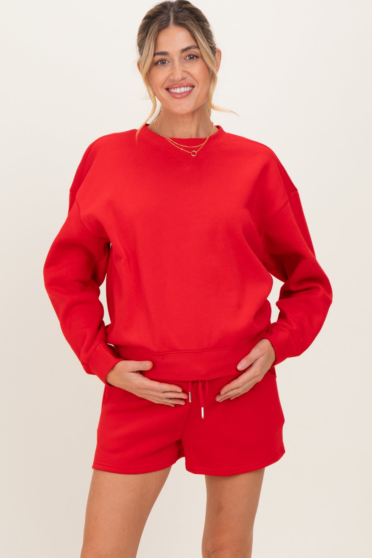 woman wearing a red maternity sweatshirt and matching shorts, holding her baby bump