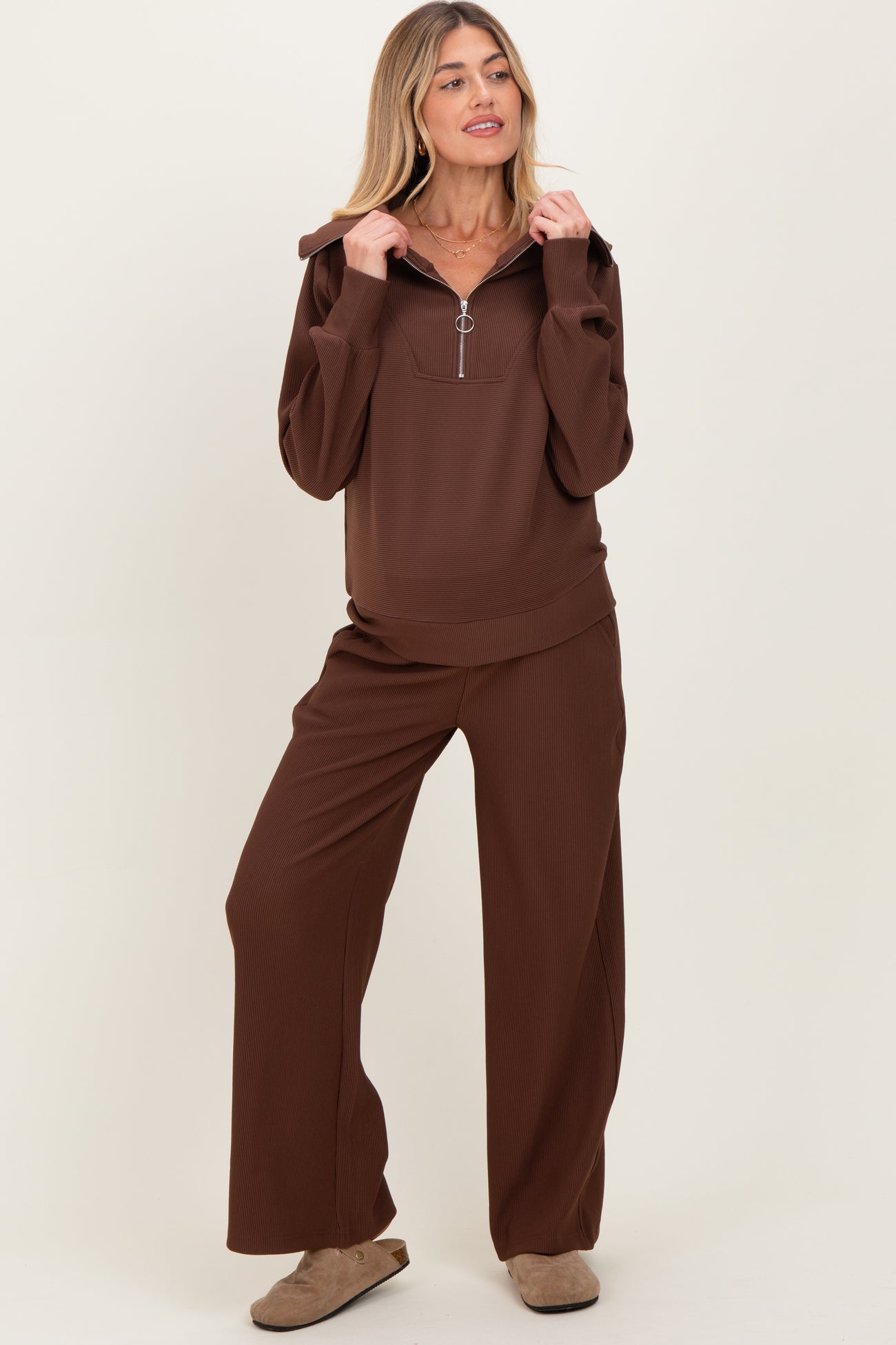 woman wearing a brown ribbed maternity loungewear set with a half-zip hoodie and wide-leg pants