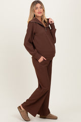woman wearing a brown maternity loungewear set with a zip-up hoodie and wide-leg pants, showing a baby bump