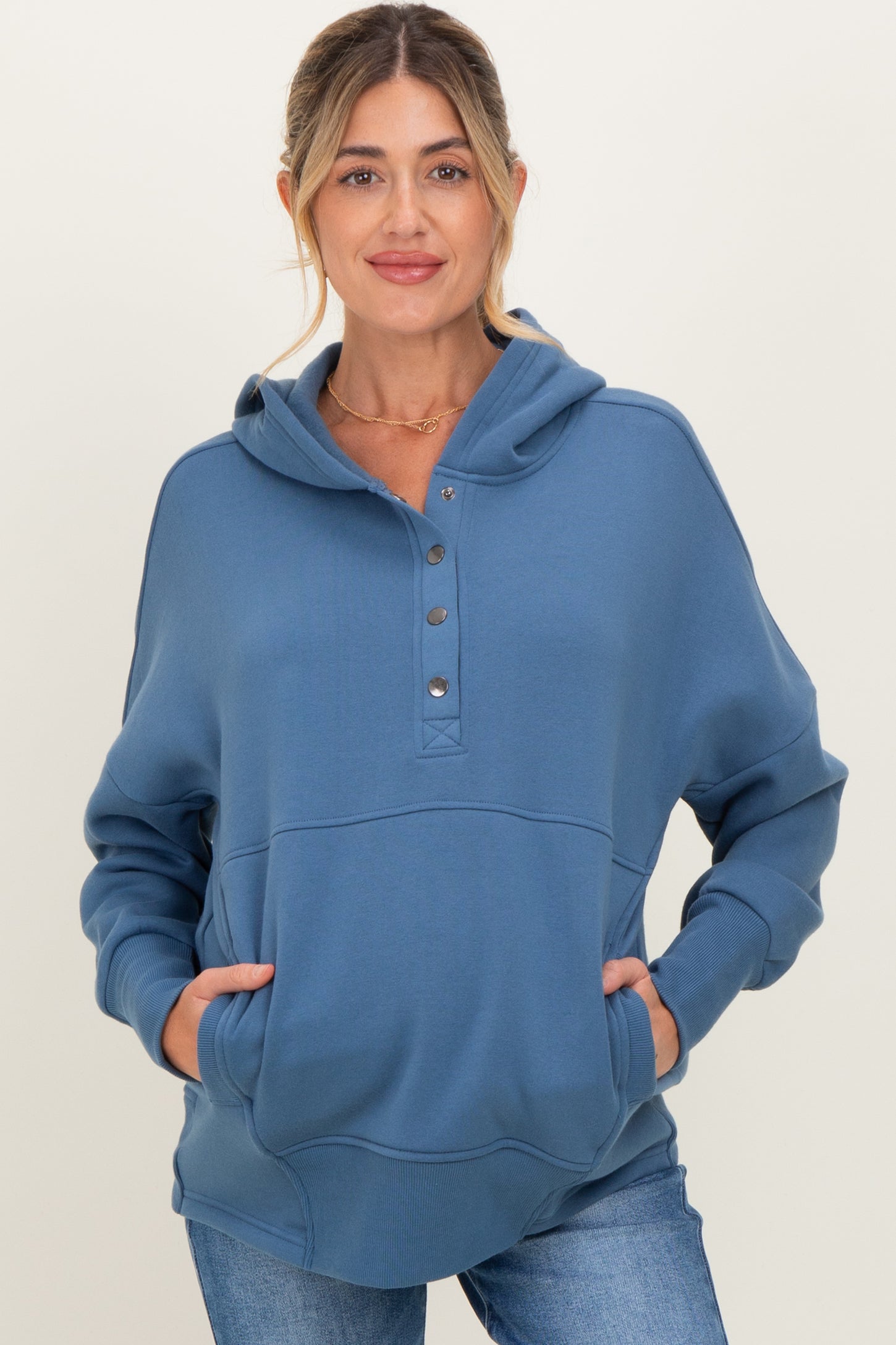 woman wearing a blue maternity hoodie with button details and front pockets, styled casually with light jeans