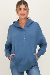 woman wearing a blue maternity hoodie with button details and front pockets, styled casually with light jeans
