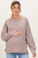 woman wearing a taupe long sleeve maternity sweater and holding her baby bump