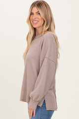 woman wearing a taupe ribbed long sleeve top with side slits and relaxed fit, smiling on a plain background