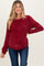 woman wearing a burgundy waffle knit maternity top and blue jeans with a visible baby bump