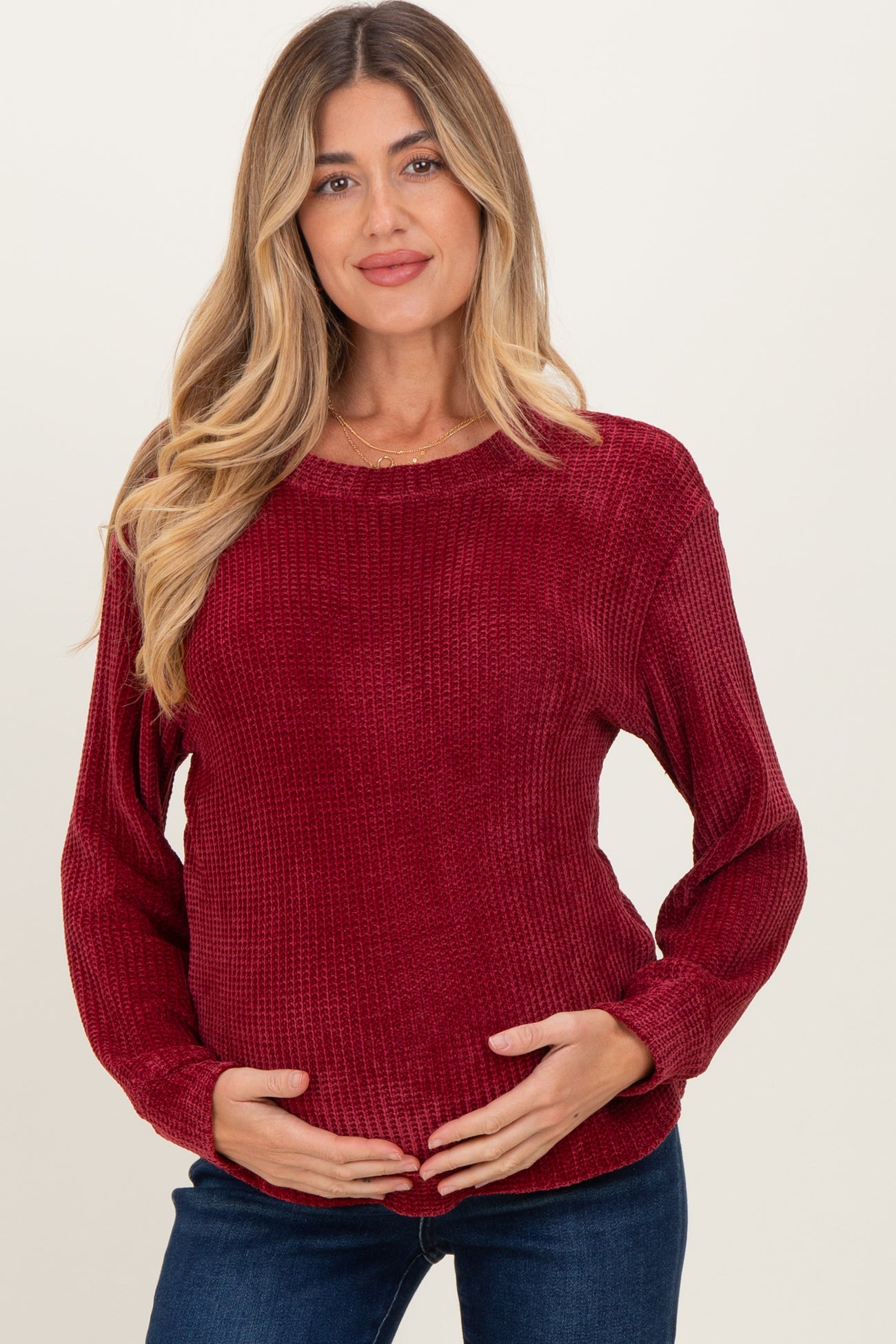 woman wearing a burgundy maternity sweater with ribbed texture and long sleeves, holding her baby bump