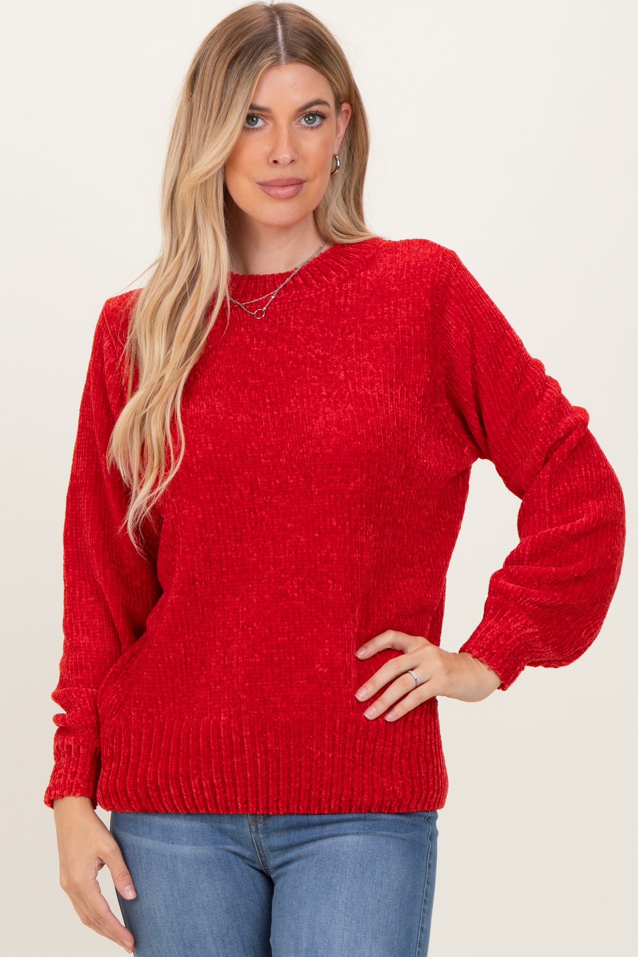 woman wearing a red knit sweater with puffed sleeves and ribbed details, paired with blue jeans