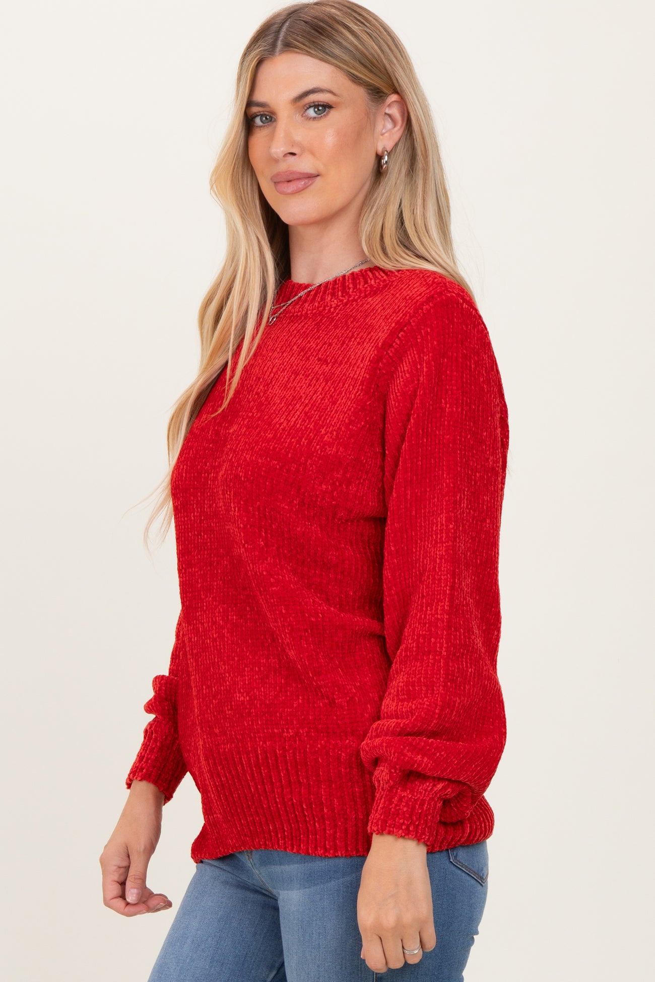 woman wearing a red textured knit sweater with puffed sleeves and a relaxed fit, paired with blue jeans