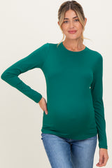 woman wearing a green long sleeve maternity top showcasing her baby bump paired with blue jeans
