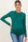 woman wearing a green long sleeve maternity top showcasing her baby bump paired with blue jeans