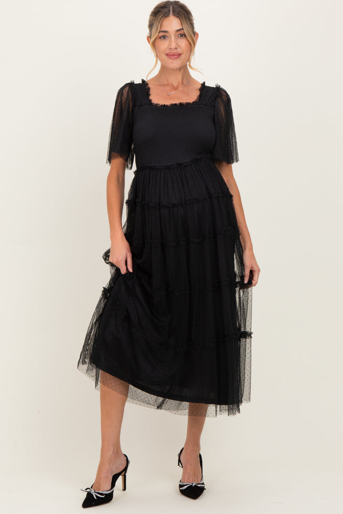 woman wearing a black maternity dress with puff sleeves and tiered tulle detailing, showing her baby bump