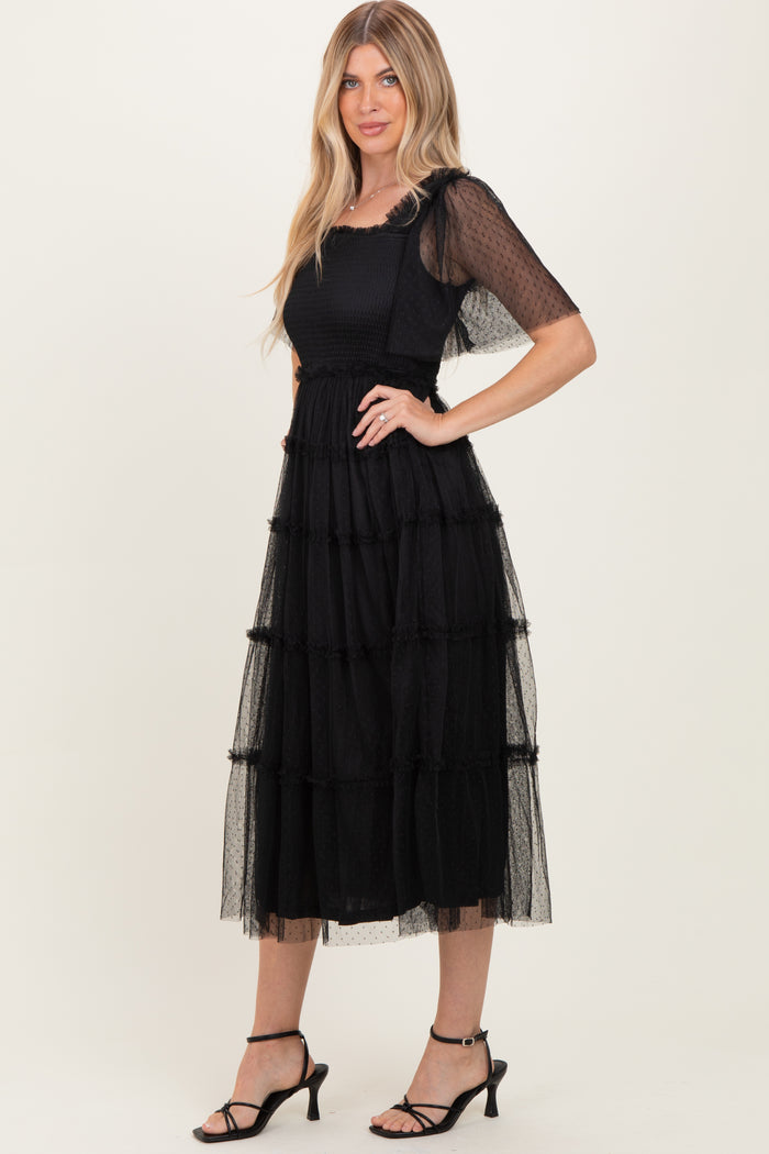 woman wearing a black tiered midi dress with sheer sleeves and a textured bodice, styled with black heels