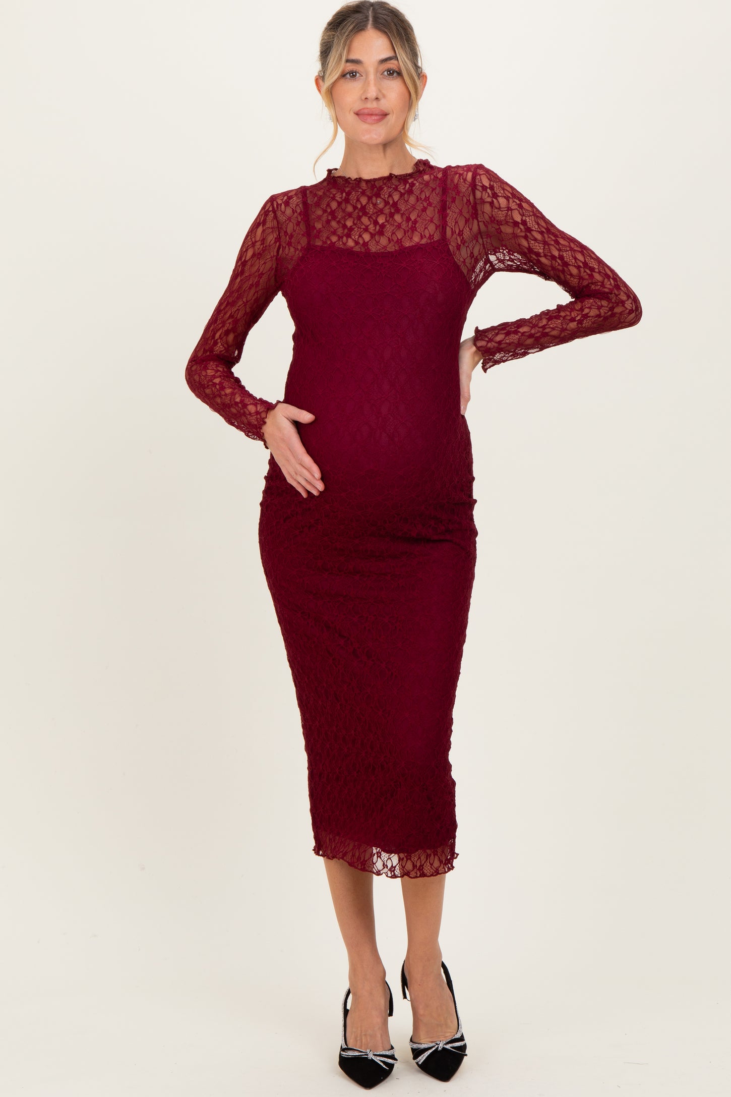 woman wearing a burgundy long sleeve lace maternity dress, gently cradling her baby bump
