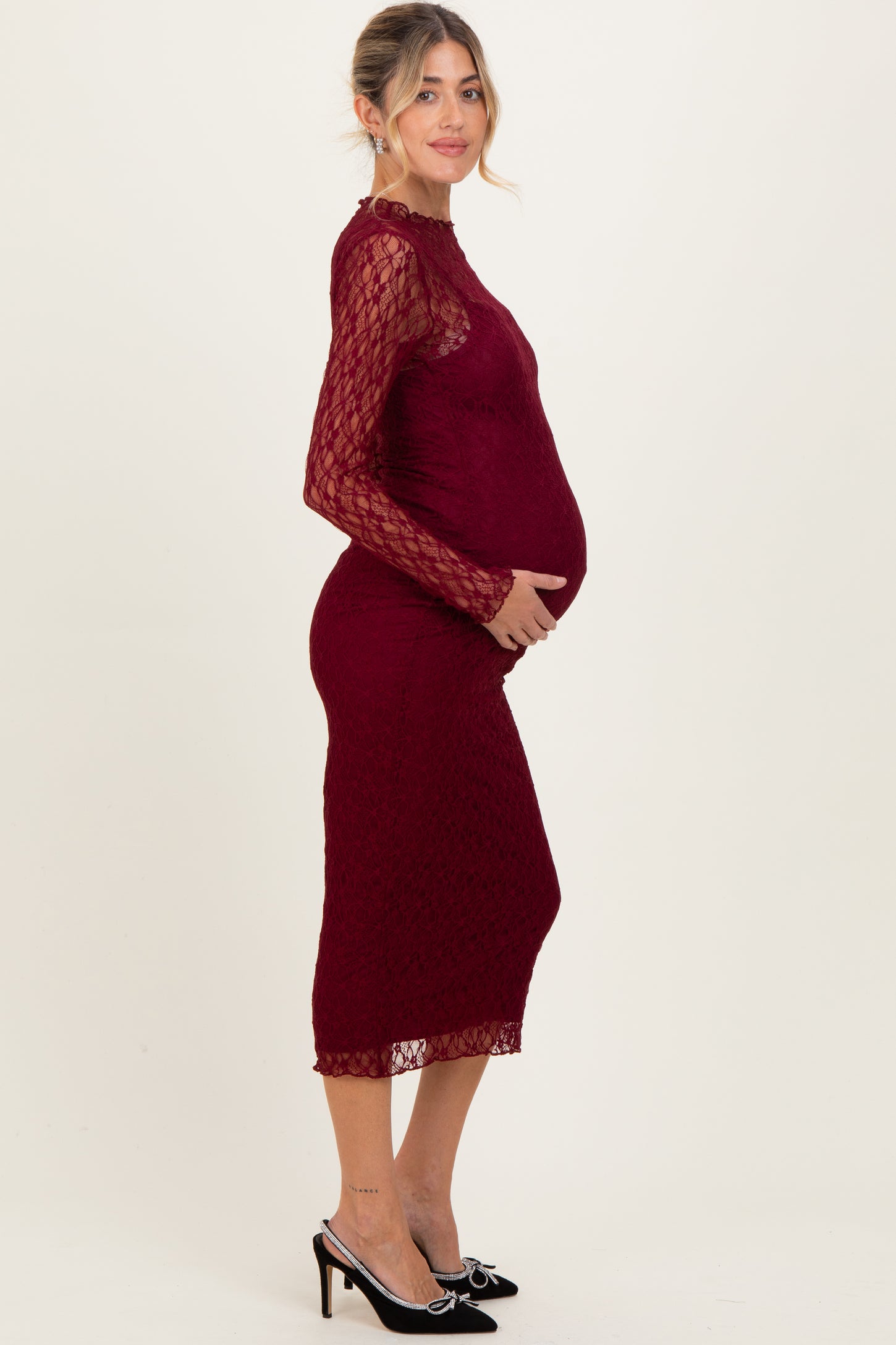 woman wearing a burgundy lace maternity dress with long sleeves and a fitted silhouette showing her baby bump