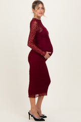 woman wearing a burgundy lace maternity dress with long sleeves and a fitted silhouette showing her baby bump