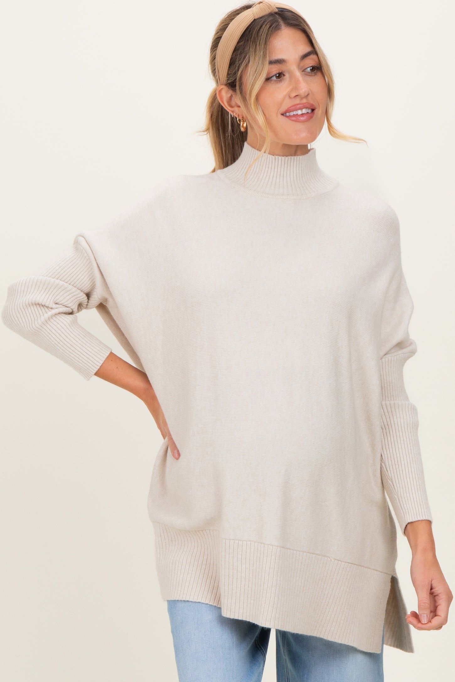 woman wearing a beige oversized turtleneck sweater, styled casually with light blue jeans