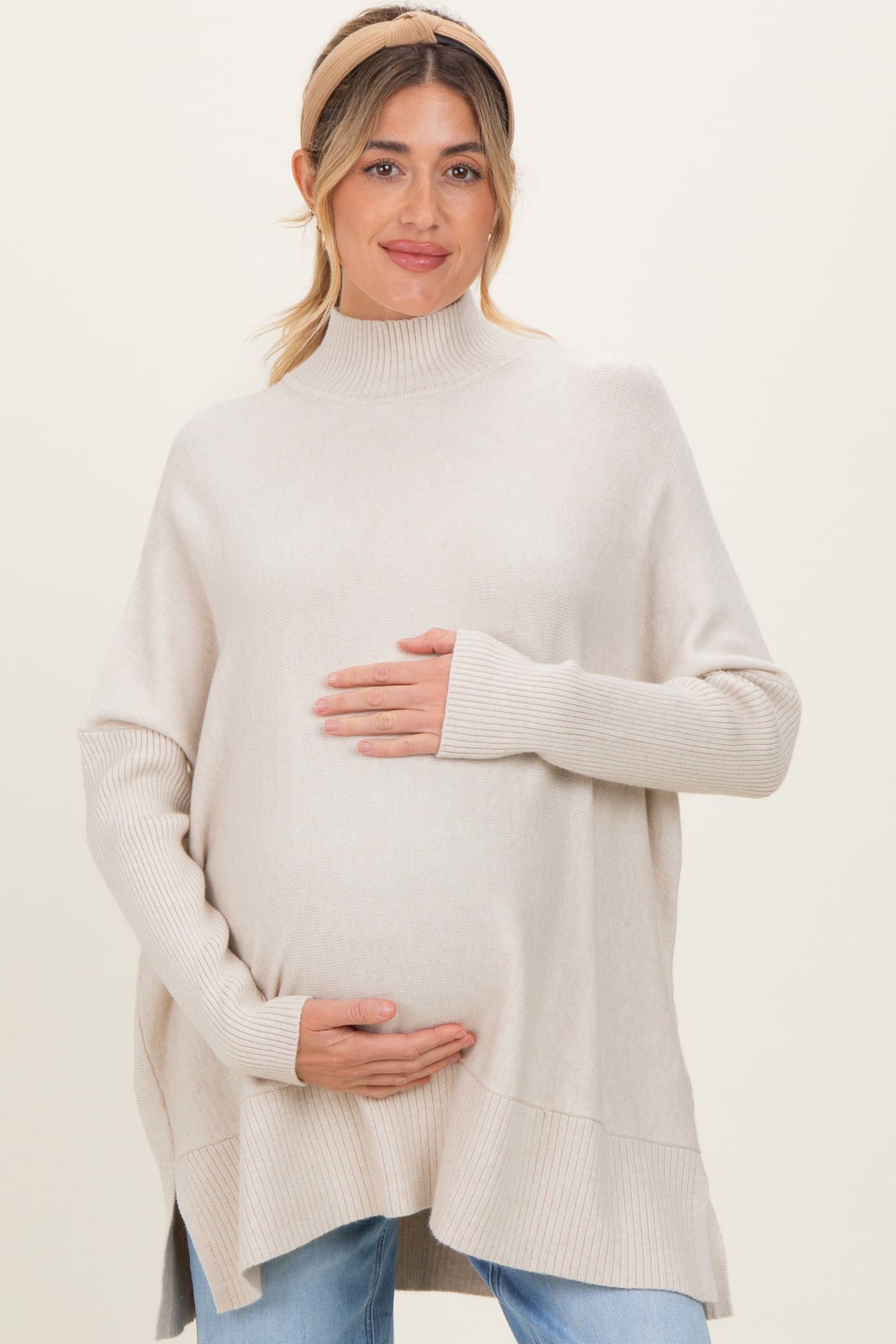 woman wearing a soft beige maternity poncho sweater and holding her baby bump