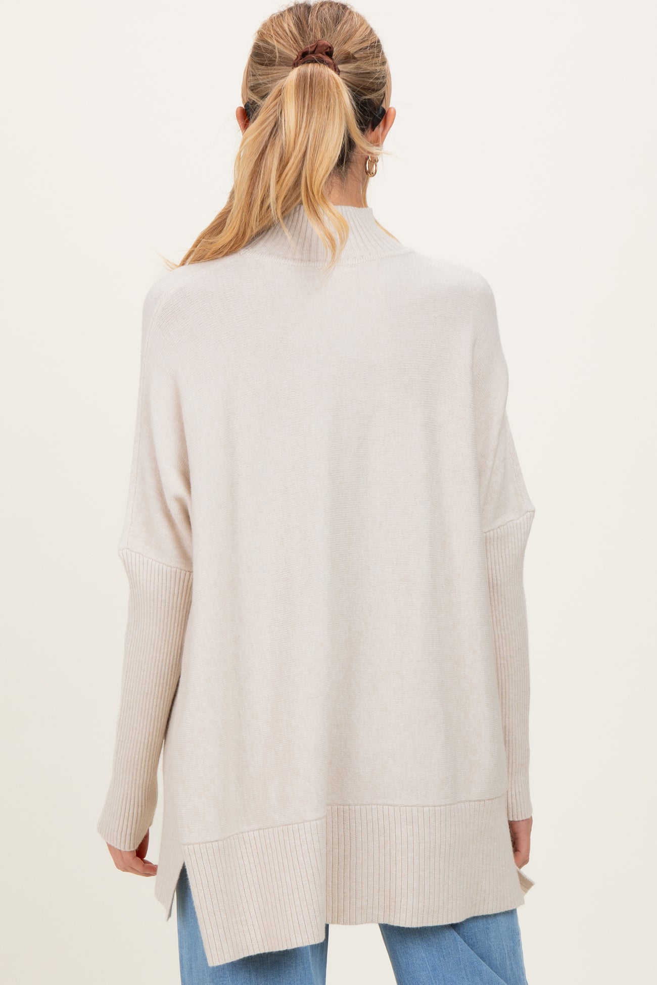 woman wearing a light beige maternity sweater with a relaxed fit and ribbed detailing, seen from the back
