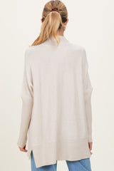 woman wearing a light beige maternity sweater with a relaxed fit and ribbed detailing, seen from the back