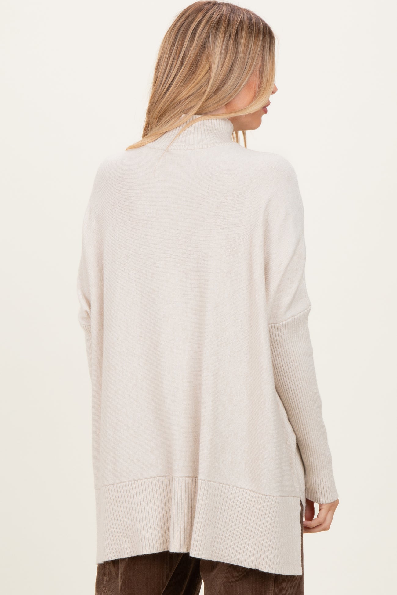 woman wearing a cream oversized turtleneck sweater with ribbed detailing and a relaxed fit from the back