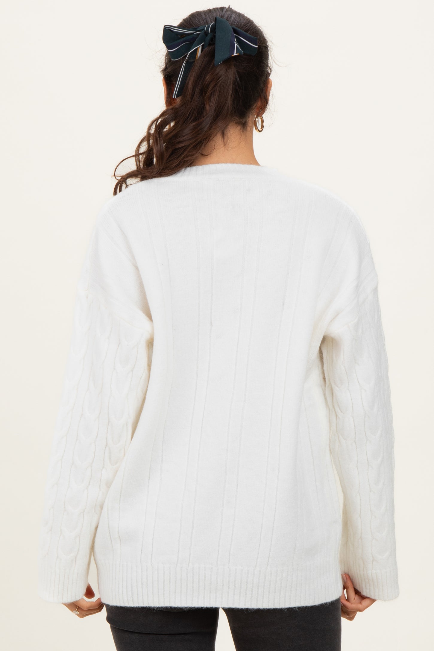 woman wearing a white cable knit sweater with a relaxed fit and long sleeves, shown from the back
