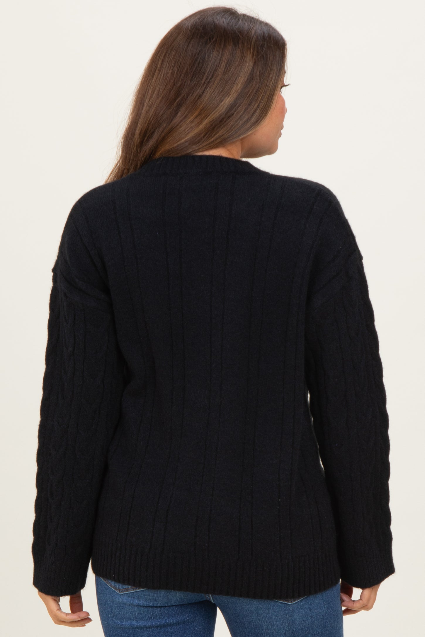 woman wearing a black cable knit maternity sweater, view from the back, showing long sleeves and relaxed fit