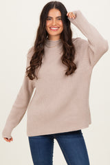 woman wearing a beige ribbed knit sweater with a high neck and long sleeves, smiling in front of a light background