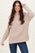 woman wearing a beige ribbed knit sweater with a high neck and long sleeves, smiling in front of a light background