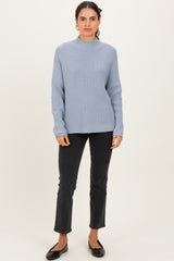 woman wearing a light blue ribbed sweater with long sleeves and black jeans, standing in a casual pose