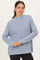 woman wearing a light blue ribbed sweater with a high neckline and long sleeves, posing with a smile