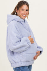 woman wearing a light purple oversized maternity hoodie, cradling her baby bump with a smile