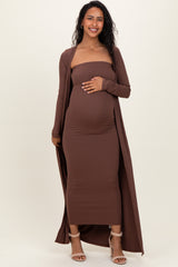 woman wearing a brown ribbed maternity dress with a long cardigan, gently holding her baby bump