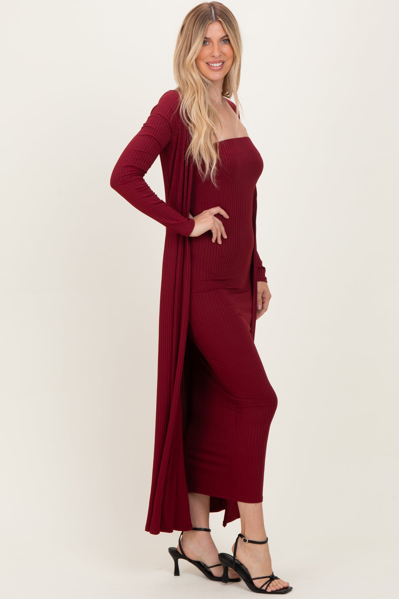 woman wearing a burgundy ribbed maxi dress with matching long cardigan and black strappy heels
