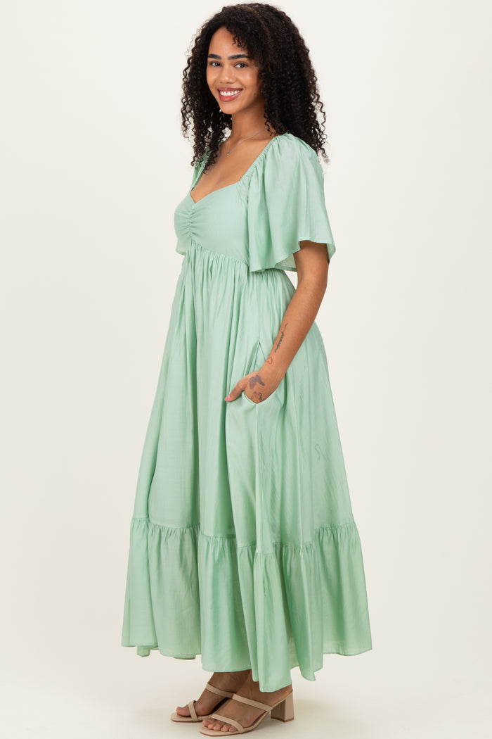 woman wearing a light green maxi dress with short sleeves and a ruffled hem, posing with hands in pockets
