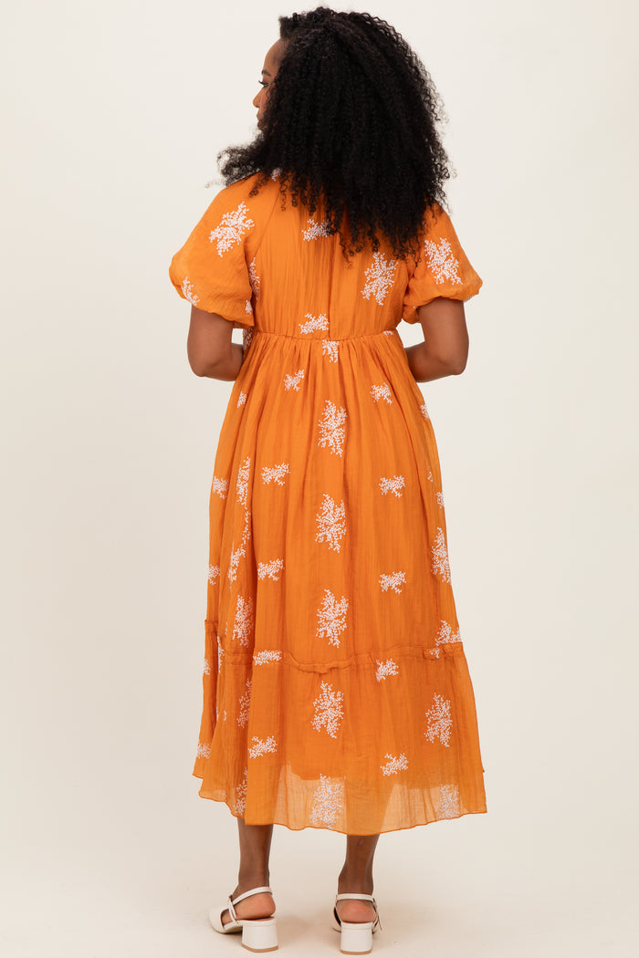 woman wearing a bright orange floral maxi dress with short puff sleeves and a tiered skirt, viewed from the back