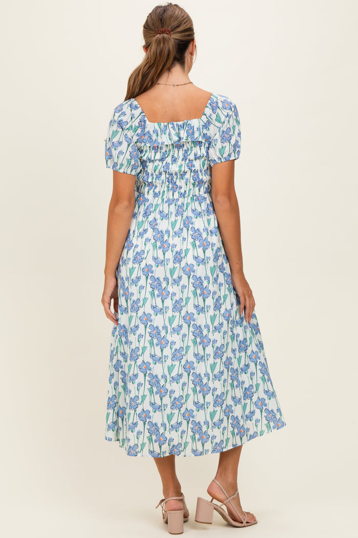 woman wearing a blue floral midi dress with short puff sleeves and a smocked back, standing with her back to the camera