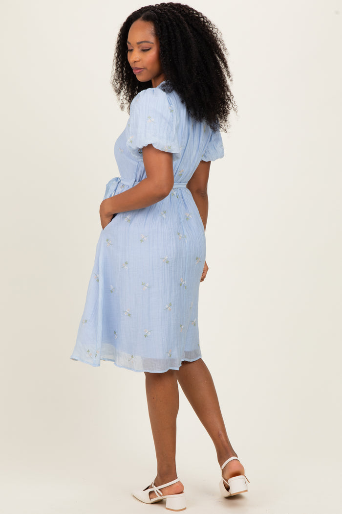 woman wearing a light blue short sleeve embroidered dress with a cinched waist and skirt detail, viewed from the back