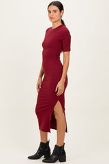 woman wearing a burgundy bodycon dress with short sleeves and a side slit, paired with black ankle booties