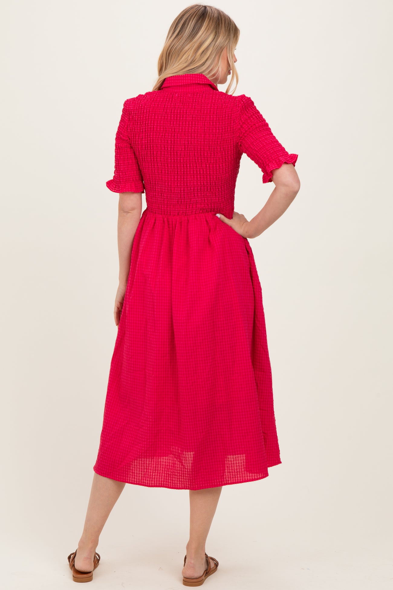 woman wearing a pink smocked midi dress with short sleeves and a button-down collar, showing the back view