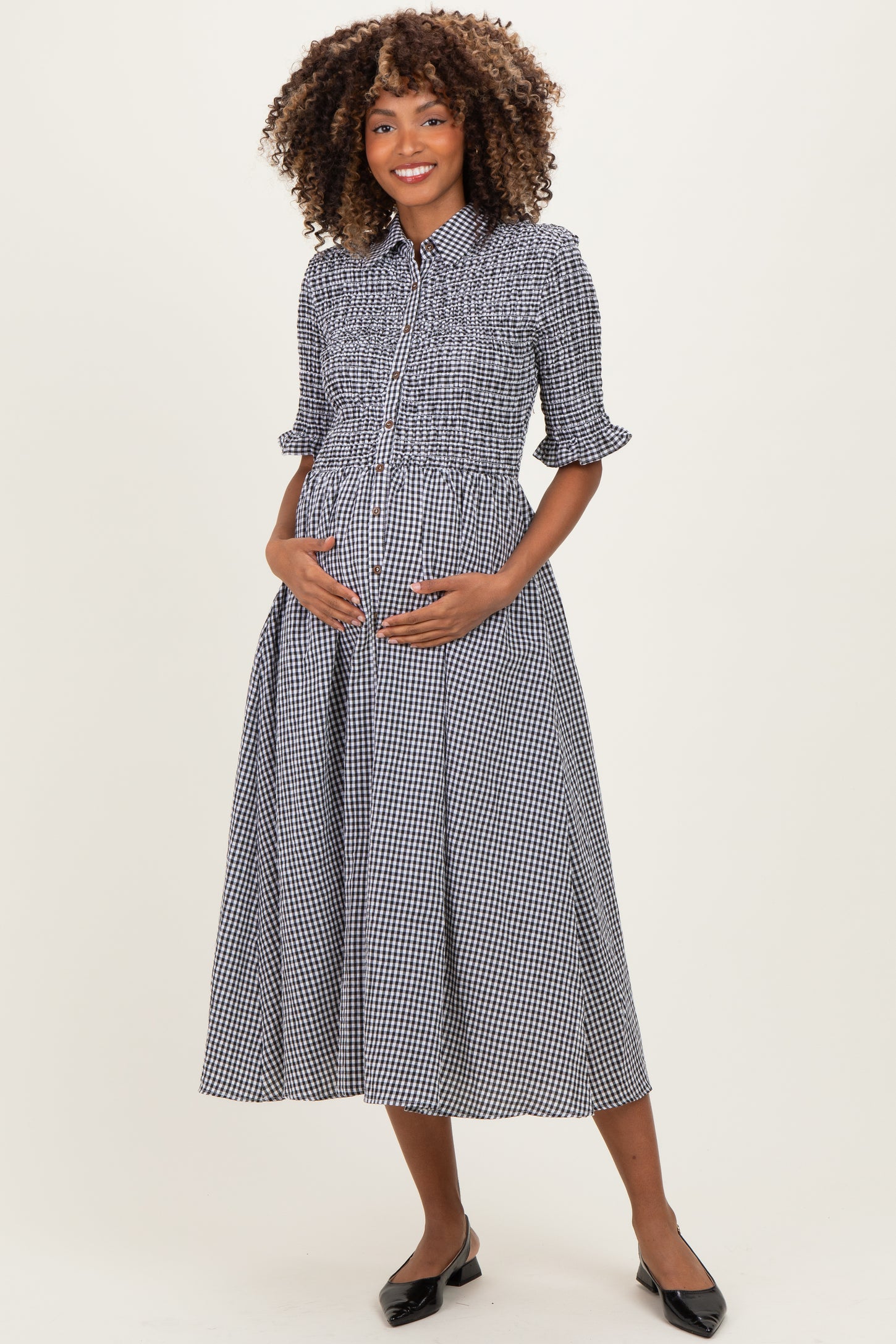 woman wearing a black and white checkered maternity dress with puff sleeves and a smocked bodice, holding her baby bump