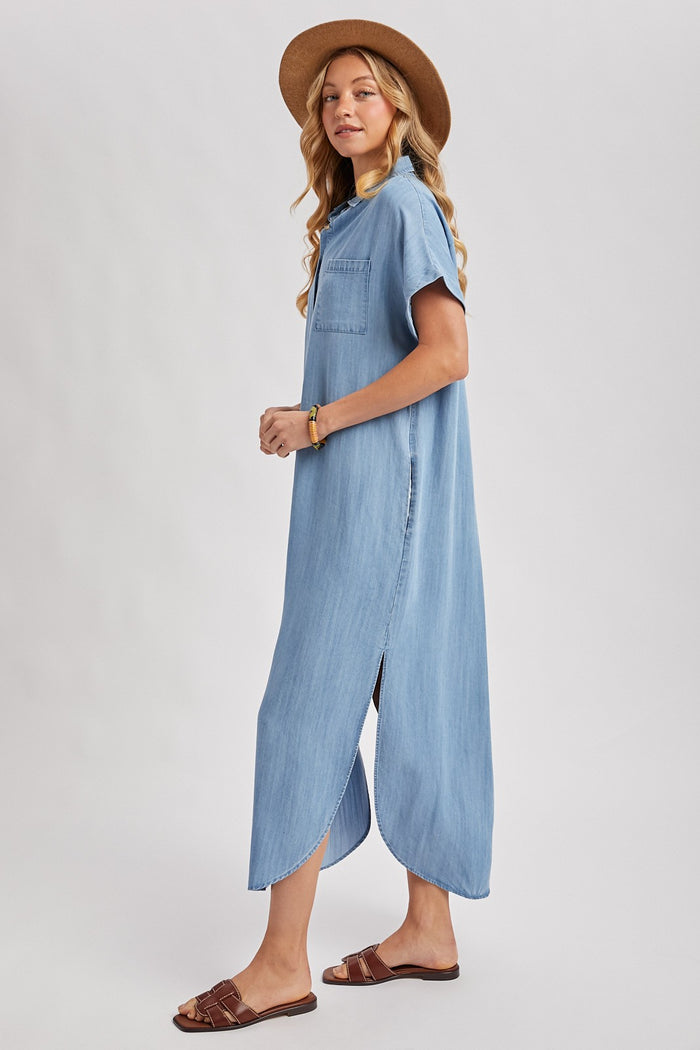 woman wearing a light blue denim maxi dress with short sleeves and a side slit, styled with a brown hat and sandals
