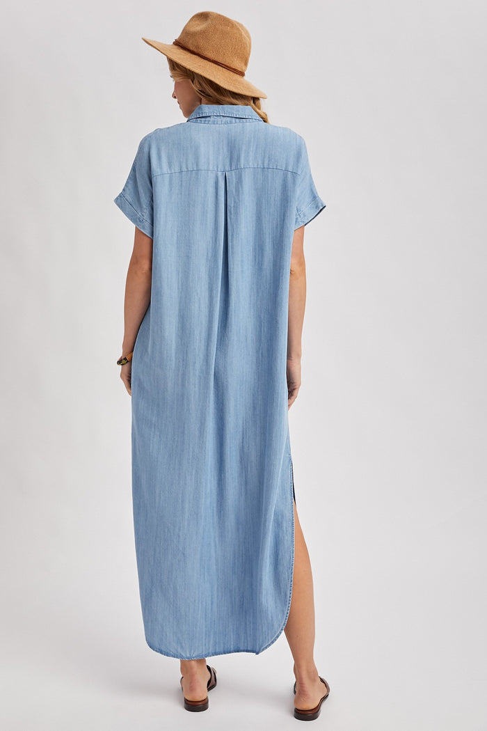 woman wearing a long denim shirt dress with short sleeves and side slits, styled with a tan hat and sandals
