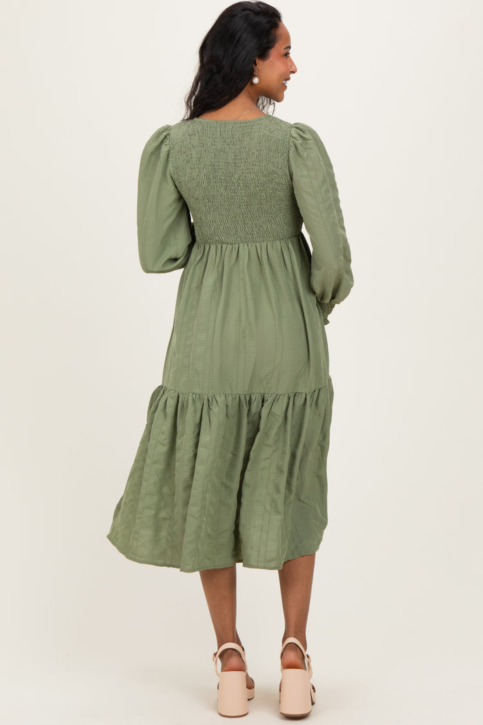 woman wearing an olive green maternity dress with puff sleeves and a tiered skirt, showing a baby bump from the back