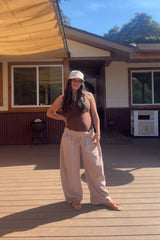 woman wearing a brown maternity tank top and loose beige maternity pants, showing baby bump, standing outdoors