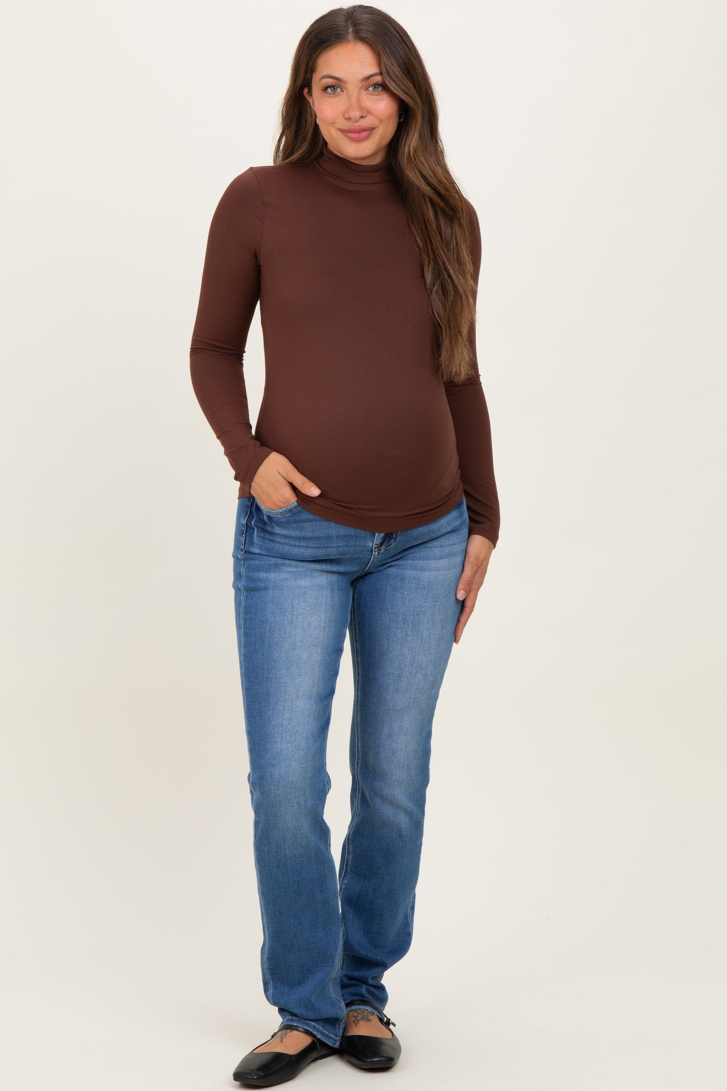 woman wearing a brown long sleeve maternity top and blue jeans with a visible baby bump